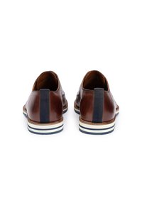 Brune lædersko med et tekstureret design, marineblå stofaccents og en kontrasterende stribet sål. Baghjørnet viser elastiske detaljer ved hælen.