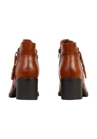 Paire de bottines en cuir marron avec talons carrés vues de dos, comprenant des détails de pompons sur le côté et des accents de coutures.