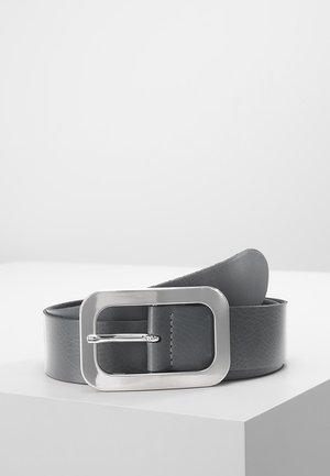 Ceinture en cuir gris foncé avec une large boucle rectangulaire en argent, placée enroulée sur une surface blanche.