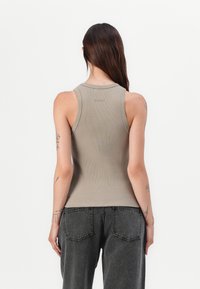 Brun ribbet tanktop med rund utringning og et enkelt design, med en liten logo på øvre del av ryggen. Kombinert med mørkegrå jeans.