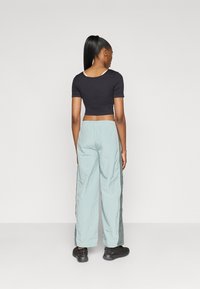 Juodas trumpas viršus su trumpomis rankovėmis, derinamas su šviesiai mėtomis plačiomis kelnių, turinčiomis šonines juostas. Modelis vilki juodus sportinius batelius.