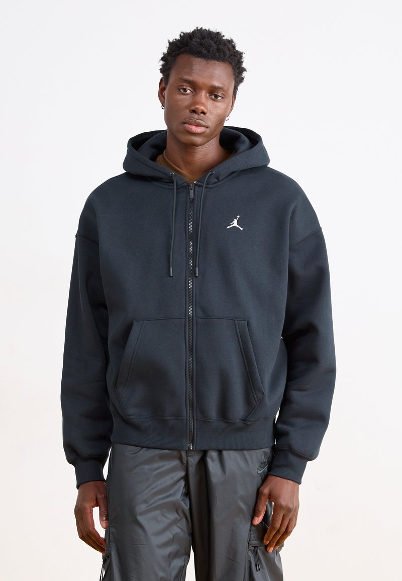 Sudadera con capucha negra con cremallera, confeccionada en mezcla de algodón, con bolsillos delanteros, capucha con cordón ajustable y un pequeño logo blanco de Jordan en el pecho izquierdo.