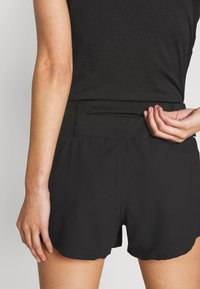 Black athletic shorts with an elastic waistband, featuring a small zippered pocket at the back and a smooth, lightweight fabric.