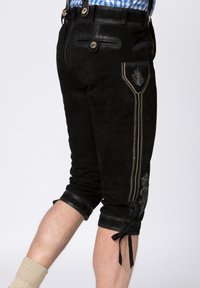 Black suede lederhosen with decorative stitching, a side pocket detail, and leather accents. Rolled hem with bows at the cuff.