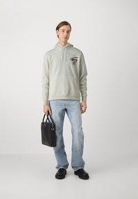 Lichtgrijze hoodie met kangoeroezak, geborduurd ontwerp, gecombineerd met lichtblauwe flare jeans en zwarte tote bag. Soepele stof en relaxte pasvorm.