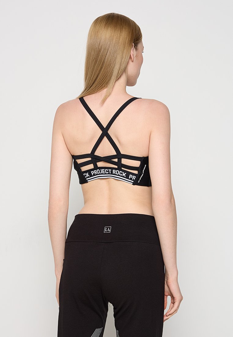 Sostenedor deportivo negro con espalda de malla, que presenta un diseño intrincado de tirantes y detalles del logo a lo largo de la banda. Tela suave y elástica.