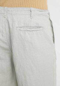Jasnoszare spodnie z lnu z klasycznym stanem, frontowymi kieszeniami oraz tylną kieszenią naszywaną. Gładka tekstura i swobodny krój.