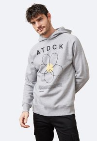 Sudadera gris con un gran diseño gráfico floral y texto. El material es suave, con un ajuste holgado y un bolsillo tipo canguro.