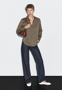 Camicia verde oliva abbottonata, vestibilità rilassata; jeans a gamba larga blu scuro; ballerine bianche; porta una piccola borsa bordeaux. Tessuto semplice e texturizzato.