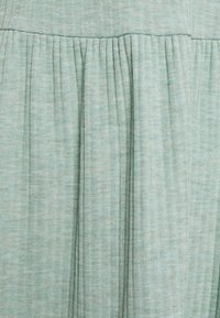 Vaalean vihreä poimutettu kangas, jossa on teksturoitu kuvio, esittäen pystysuoria viivoja ja hienovaraisia värivaihteluita pinnalla.