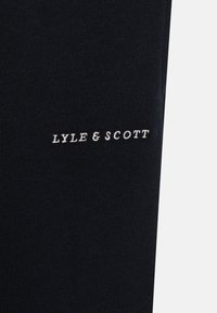 Tissu bleu marine à texture lisse avec broderie blanche "LYLE & SCOTT" positionnée le long du bord inférieur.