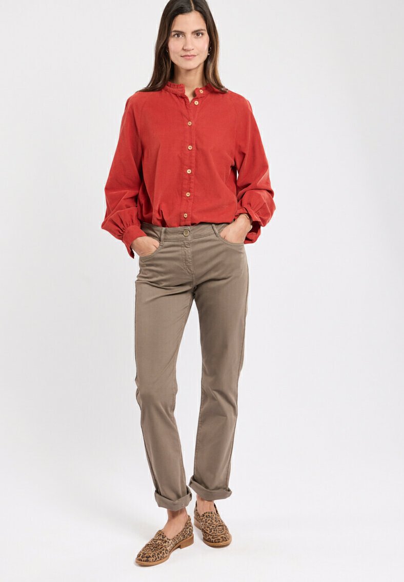 Chemise rouge à boutons avec un col haut, pantalon slim beige, et chaussures marron à imprimé léopard. Le tissu semble doux avec des manches retroussées.