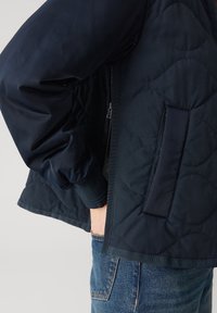 Marine gewatteerde jas met ritssluiting, ribgebreide manchet en een zijzak, met een gestructureerde afwerking en gladde stof.