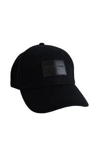 Gorra de béisbol negra de tela con visera curva. Presenta una placa rectangular de cuero negro con el relieve "TOMMY HILFIGER."