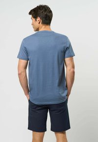 Granatowy t-shirt z krótkim rękawem, miękka faktura, dekolt w łódkę, noszony z ciemnymi szortami, widziany od tyłu, z subtelnymi detalami szwów.