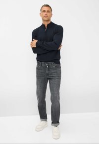 Maglione blu navy a maglia con colletto a mezza zip abbinato a jeans grigi slim-fit. Sneakers bianche completano l'outfit. Design semplice e moderno.