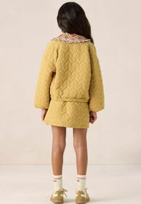 Veste matelassée jaune avec un col à motif rose, assortie à une jupe coordonnée. L'ensemble présente des manches longues et une coupe décontractée.