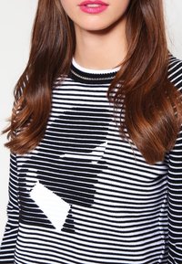 Maglione a righe bianche e nere con scollatura rotonda, caratterizzato da un grande motivo astratto al centro, realizzato in materiale lavorato a maglia.