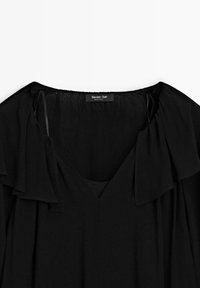 Svart blus med V-ringning och draperade volangärmar. Slät textur, lätt tyg och en subtil lyster. Etikett: Massimo Dutti.