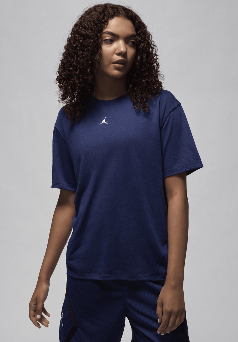 Camiseta de algodão azul-escuro com decote redondo e mangas curtas, apresentando um pequeno logótipo branco no peito. Textura suave e corte descontraído.