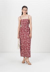 Röd och vit blommönstrad klänning med spagettiband, figurnära liv och lång kjol. Matchad med en vit handväska och beige klackar.