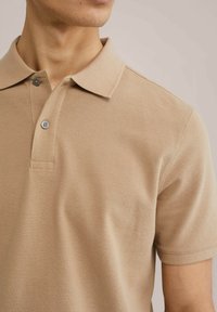 Camisa polo beige con un tejido texturizado, manga corta, un cuello clásico y detalle de tapeta con dos botones.