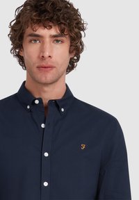 Marine blauwe button-down shirt van katoen, met een kraag, witte knopen en een oranje geborduurd logo op de linker borst.