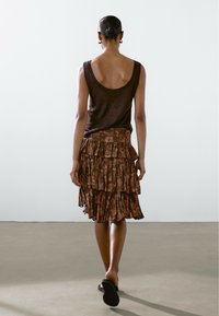Top in cotone marrone con scollo a barca, abbinato a una gonna marrone a strati con volant e motivo floreale, e sandali neri.