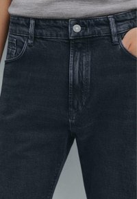Jeans in denim scuro con un classico design a cinque tasche, una texture liscia e dettagli di cucitura sottili, con chiusura a bottone in vita.