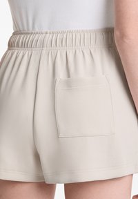 Béžové šortky s elastickým pasem, vybavené jednou zadní kapsou a hladkým, jemným materiálem. Spodní lem je zakončený čistým stehem.