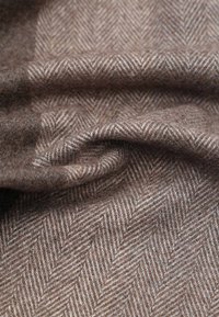 Brown herringbone fabric with a textured finish, featuring a subtle pattern of diagonal lines. Soft and pliable material, creating gentle folds.