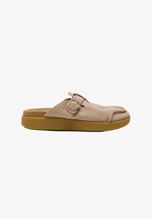 Zapato beige de ante tipo slip-on con una hebilla redonda dorada y una suela gruesa de goma marrón, mostrado de perfil.