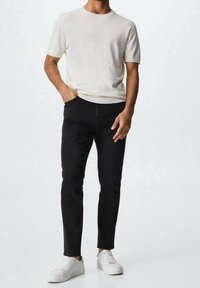 Suéter corto de manga corta en beige claro, jeans negros ajustados y zapatillas blancas. Textura suave, diseño minimalista, sin patrones visibles.