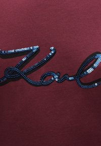 Bordo audinys su lygiu paviršiumi, ant kurio yra didelis mėlynų blizgučių užrašas "Karl". Dizainas yra centrinis, be papildomų elementų.