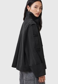 Giacca nera, oversized, con colletto alto, tessuto testurizzato e dettagli unici sulle spalle. Presenta ampi polsini e una vestibilità rilassata.