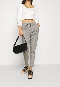 Grijze geprinte broek met een trekkoord in de taille, gecombineerd met een witte cropped top en zwarte platform sandalen. Inclusief een zwarte gestructureerde handtas.
