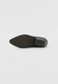 Suela de zapato de cuero negro con forma puntiaguda, agarre de goma texturizada y un acabado suave. Presenta líneas sutiles cerca del talón y acentos en los laterales.