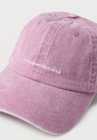 Πλυμένο ροζ καπέλο μπέιζμπολ με λευκό κεντημένο κείμενο "no expectations" στο εμπρόσθιο πάνελ, σε λευκό φόντο.