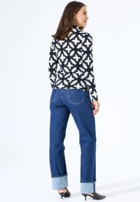 Langemouwen top met een zwart-wit zigzagpatroon, gecombineerd met hooggesneden blauwe jeans met omgeslagen boorden en zwarte muiltjes.