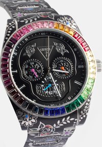 Schwarze Uhr mit einem Totenkopfdesign auf dem Zifferblatt, gravierten Blumenmustern am Armband und einem mehrfarbigen mit Edelsteinen besetzten Gehäuse.