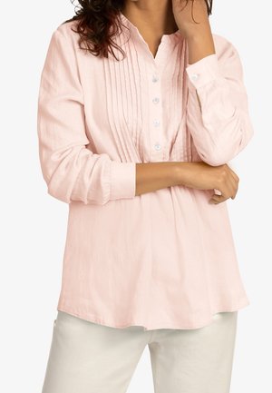 Chemise longue à manches longues de couleur rose pâle, ornée de pinces sur le devant, d'un col montant et d'une fermeture à boutons. Fabriquée dans un tissu doux et texturé.
