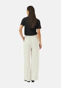 Svart kortermet skjorte kombinert med kremfargede, stripete vide bukser med avslappet passform og elastisk liv. Vist bakfra.