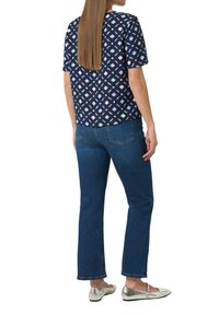 Dunkelblaues Kurzarmoberteil mit einem geometrischen Muster in Hellblau und Creme, kombiniert mit dunkelblauen Jeans und metallisch silbernen Ballerinas.