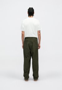 Bela kratka majica s kratkimi rokavi in olivno zelenimi žametnimi hlačami s hrbnimi žepi, prikazane s hrbtne strani. Celo tekstura in sproščen kroj.