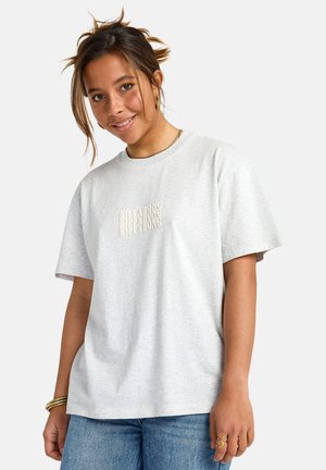 Camiseta de algodón gris con mangas cortas, que presenta un diseño de logotipo texturizado y en relieve en color crema en la parte delantera. Ajuste casual con escote redondo.