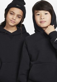 Due bambini indossano felpe nere abbinate con tasche frontali e cordini. La ragazza ha un'acconciatura con treccia e un berretto; il ragazzo ha i capelli corti.