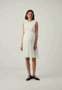 Rochie albă până la genunchi cu un tors din material texturat, talie elastică și fustă evazată. Asortată cu pantofi negri tip slip-on și accesorii minime.