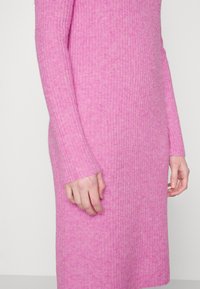 Rosa ribbad tröjklänning med långa ärmar och en rak silhuett. Mjuk textur, med ett subtilt mönster och åtsittande mudd.