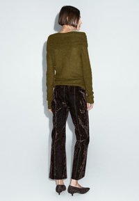 Maglione verde oliva off-shoulder con dettagli a coste, abbinato a pantaloni in velluto scuro caratterizzati da una texture liscia e una lunghezza cropped.