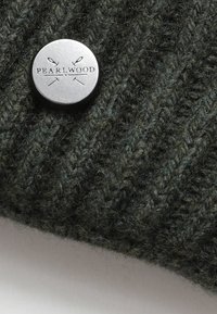 Tamsiai žalias mezginys su raukšlėta tekstūra, su metaliniu mygtuku, įrašytu "PEARLWOOD" ir kryžminiu adatom.